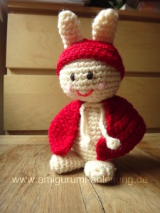 Der Amigurumi-Hase hat einen Mantel und eine rote Mütze.